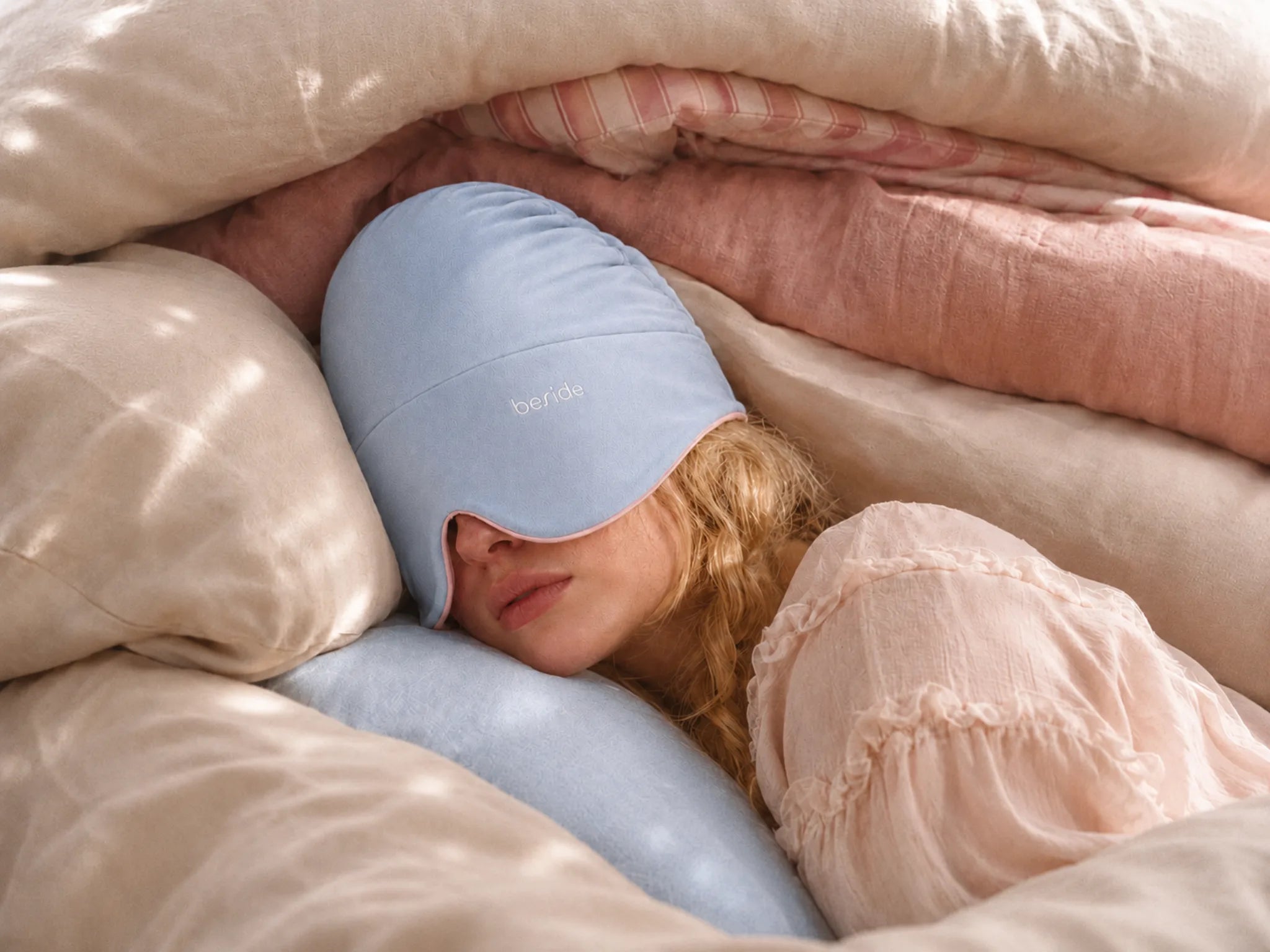 A woman resting under soft bedding, wearing the Beside sleep hood